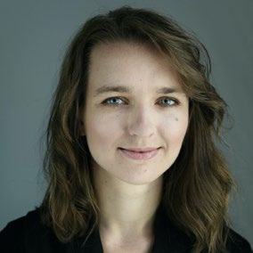 Headshot of a woman with long, wavy brown hair and blue eyes, smiling faintly.