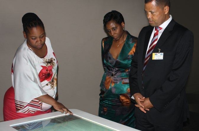 Three people, two women and one man, gather around and look at an interactive display screen.
