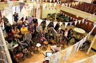 A large group of people gathered indoors, seated and standing, under decorative bunting.