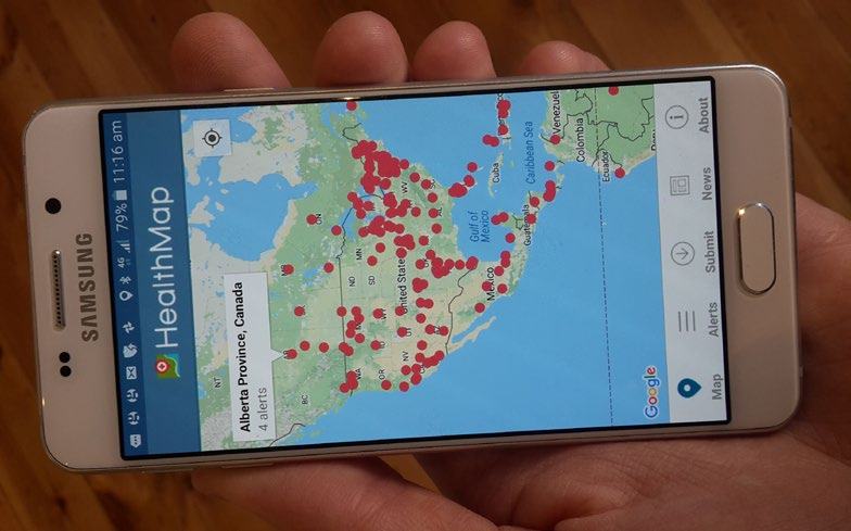 Screenshot of a "HealthMap" app on a smartphone, showing North America with red dots indicating health alerts, with Alberta Province, Canada highlighted.