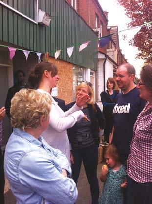 A group of people, including adults and a child, gathered outdoors in front of a building with bunting, appearing to be at a community event.