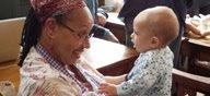 An older woman smiling affectionately at a baby reaching out to her, depicting intergenerational interaction.