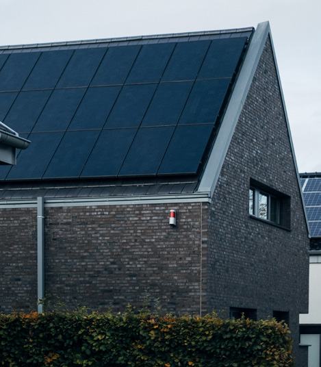 A modern dark brick house with its entire roof covered by an array of black solar panels.