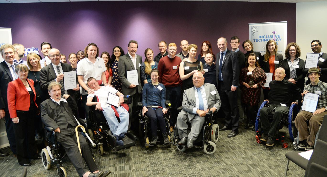 Group photo of people, some in wheelchairs, holding certificates and awards at an "Inclusive Technology" event.