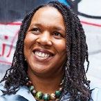 Headshot of a smiling Black woman with braided hair and a patterned necklace.