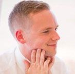 Headshot of a smiling white man with short hair, thoughtfully touching his chin.