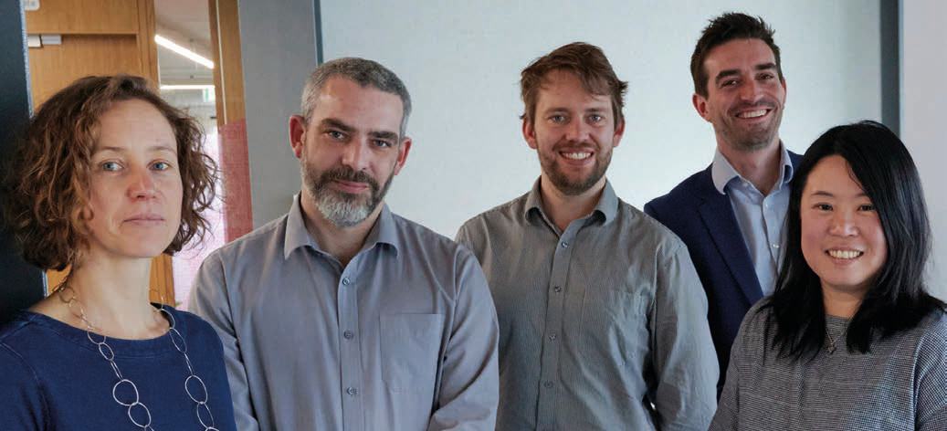 Photo of five individuals, likely a professional team, standing together and smiling.