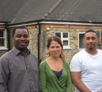Three smiling people, two men and one woman, standing outdoors in front of a brick building.