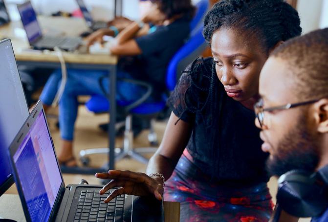 Two people, a woman and a man, collaborating and looking at a laptop screen in a modern office environment.