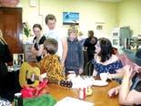 Group of young people gathered in a casual room, some sitting at a table with a guitar, others standing and conversing.