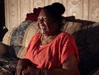 An older woman sitting on a sofa, laughing joyfully, conveying a sense of happiness and well-being.