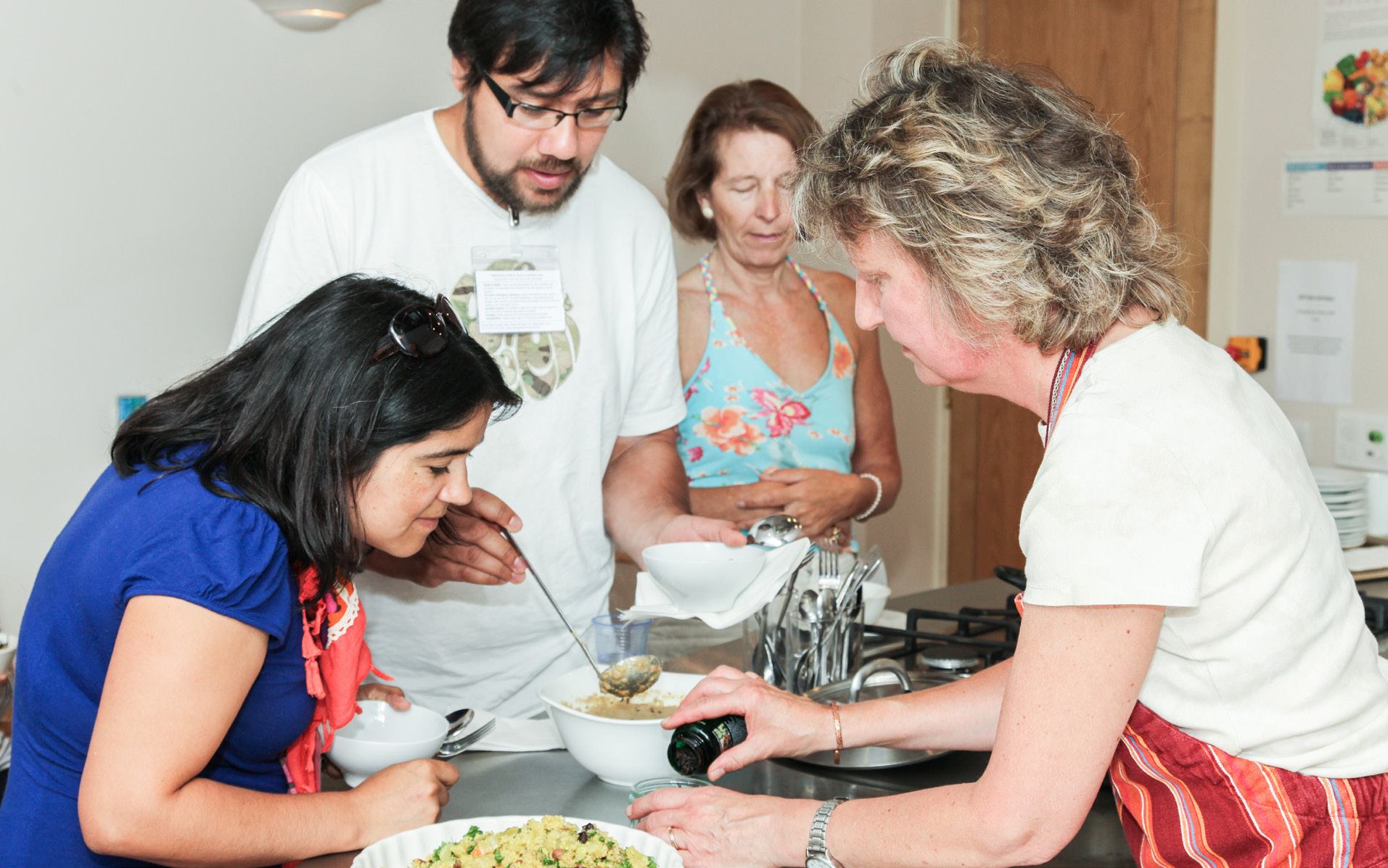 Four people participating in a cooking class or session in a kitchen, preparing food together.