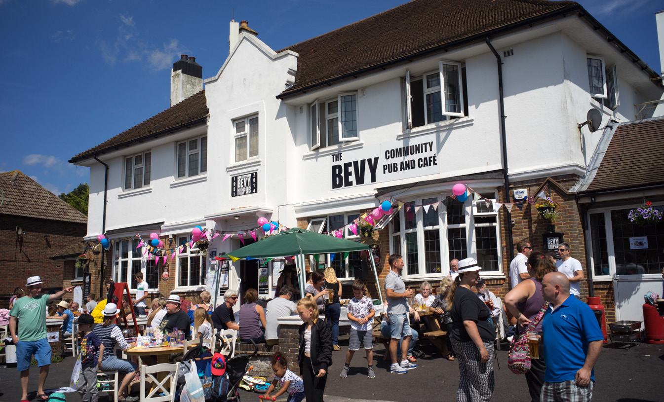 The exterior of "THE BEVY COMMUNITY PUB and CAFÉ" with many people gathered enjoying an outdoor event.