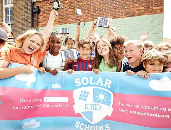 Diverse group of excited children holding a banner for 'Solar Schools' and small solar panels, promoting fundraising for a solar roof.