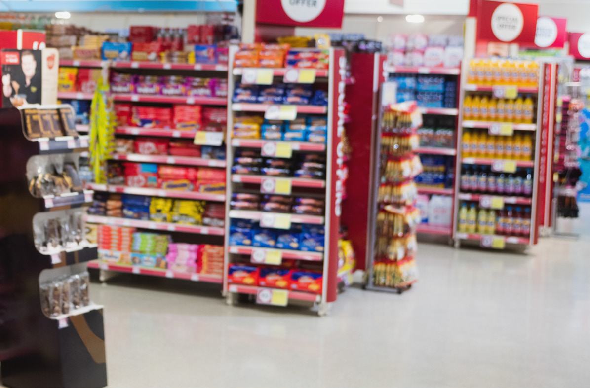 A blurred, wide shot of a supermarket interior, showing multiple aisles with shelves stocked with various products.