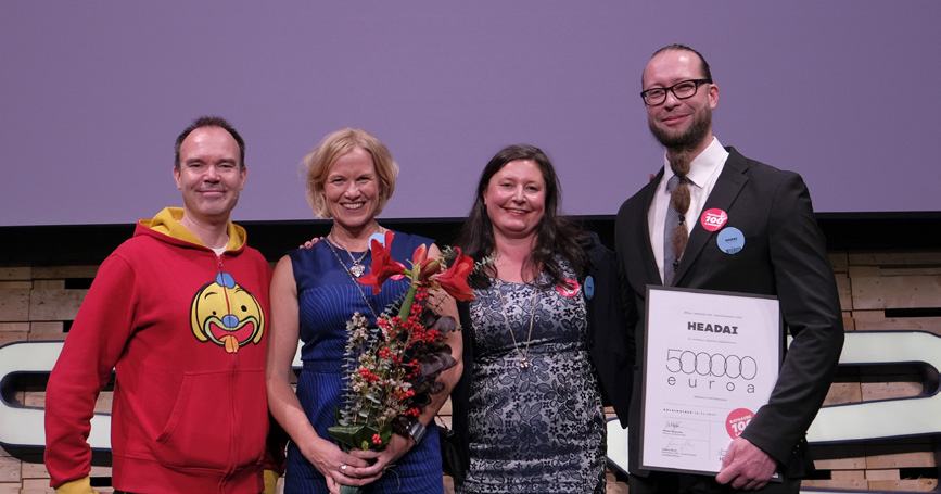 Four people, three women and one man, on a stage. The man holds an award certificate for 500,000 euros from HEADAI.