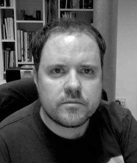 Black and white close-up portrait of a man with a beard and short hair, looking directly at the camera.