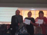 Three people, two women and a man, standing and holding up certificates during an awards or recognition ceremony.