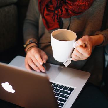 Hands holding a white mug with a tea bag, resting on a laptop keyboard.