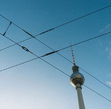 The Berlin TV Tower against a blue sky, with power lines crisscrossing in the foreground.
