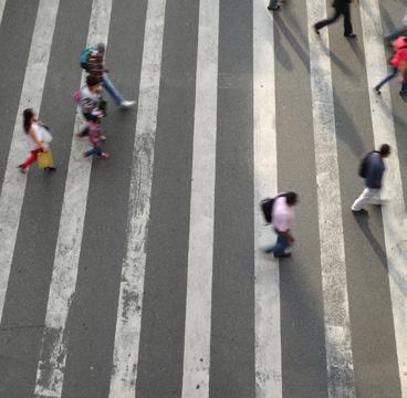 An overhead view of several people crossing a white-striped zebra crossing on an asphalt road.