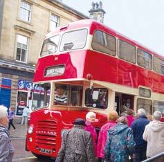 A vintage red double-decker bus parked on a street with several people standing near its entrance, appearing to board or disembark.