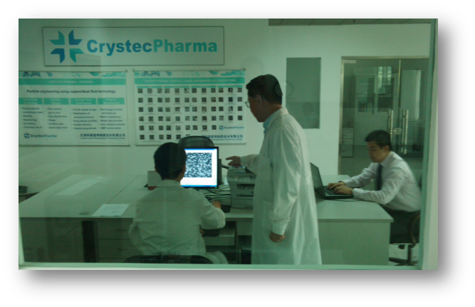 Three scientists in a lab; two examine a microscope image on a monitor, one works on a laptop. CrystecPharma logo and technical charts are on the wall.