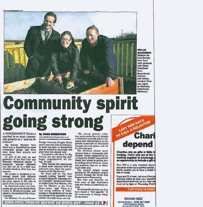 Newspaper clipping showing three smiling people kneeling in a garden bed, illustrating an article titled "Community spirit going strong."