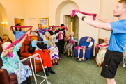 Seniors participate in a group exercise class, led by an instructor, using pink resistance bands in a common room.