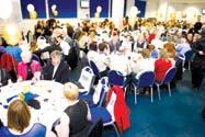 People gathered at round tables in an event hall with balloons and decorations, attending a social event.