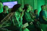 Audience members attending a presentation, sitting and listening in a green-lit room.