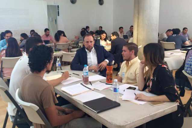 A group of people sitting at tables, engaged in discussions or a workshop, with papers and drinks on the tables.