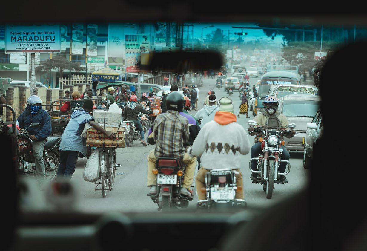 View from inside a vehicle showing a crowded street with numerous motorbikes, cars, and pedestrians in a busy city.