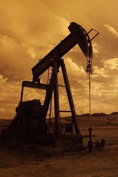 An oil pumpjack silhouetted against a cloudy, orange-tinted sky in a field.