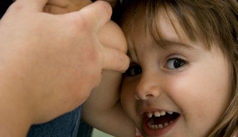Close-up of a smiling young child with missing front teeth, with an adult hand visible.