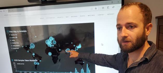 A man pointing at a large screen displaying a world map with data points and filters, visualizing global information.