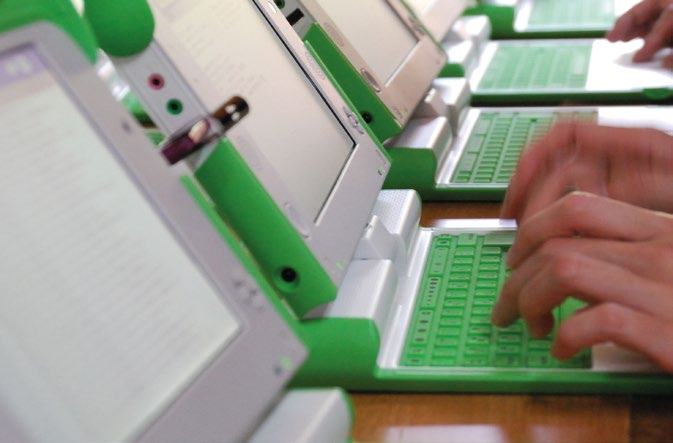 A row of green and white laptops, with hands typing on one in the foreground, suggesting a classroom or training session.