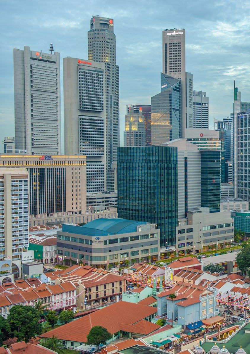 Aerial view of a city skyline showing modern skyscrapers in the background and traditional low-rise buildings with red roofs in the foreground.