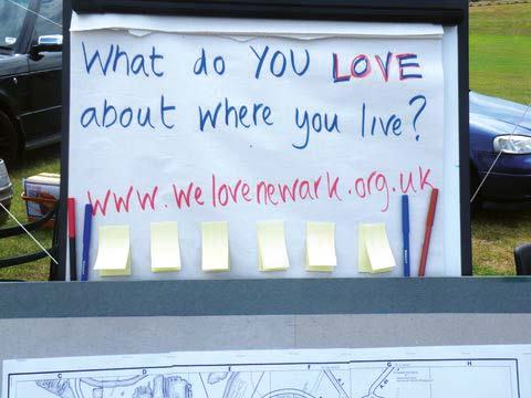 Flip chart sign asking "What do YOU LOVE about where you live?" with a website address and yellow sticky notes for responses, used for community feedback.