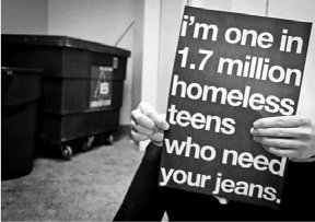 A person holding a sign stating "I'm one in 1.7 million homeless teens who need your jeans," with a dumpster in the background.