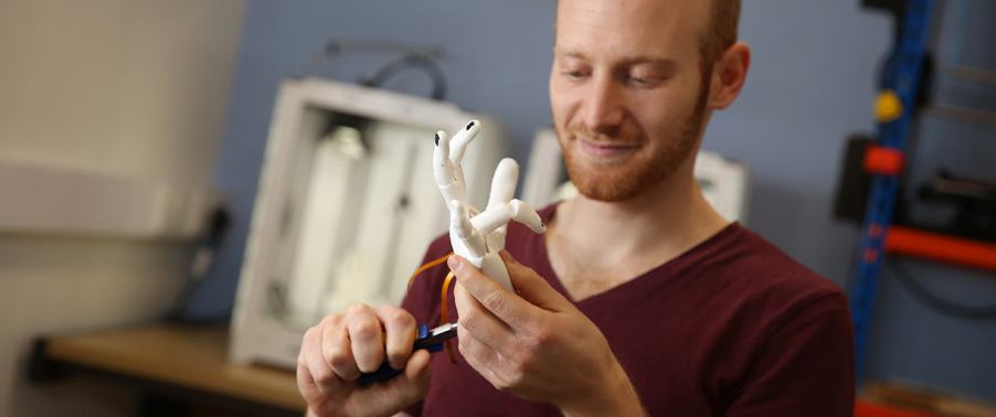 A man holding and adjusting a white 3D-printed prosthetic hand with pliers, showcasing product development or assembly.