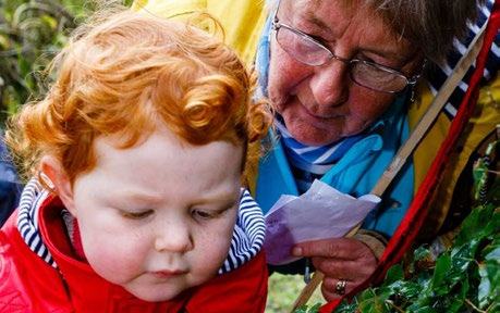 An elderly woman and a young child with red hair look intently at something on the ground, appearing to be observing nature.