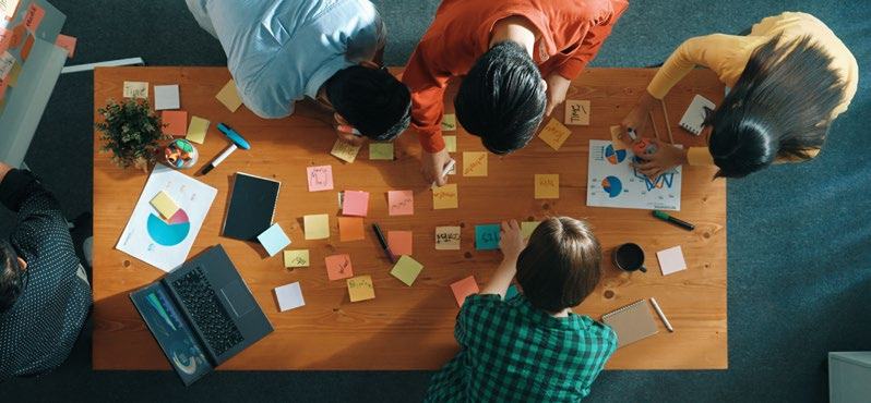 Overhead view of a team collaborating around a table with sticky notes, charts, and a laptop.