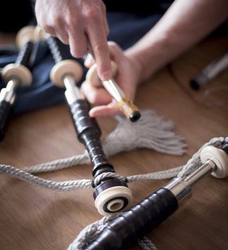 Close-up of hands adjusting or assembling parts of a set of bagpipes laid out on a wooden surface.