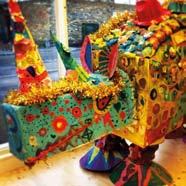 A vibrant, multi-colored rhinoceros sculpture decorated with intricate patterns, textures, and gold tinsel, likely an art installation.