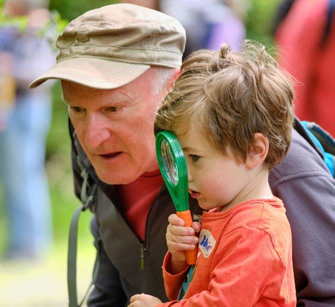 An adult man and a young boy use a magnifying glass to examine something closely outdoors.