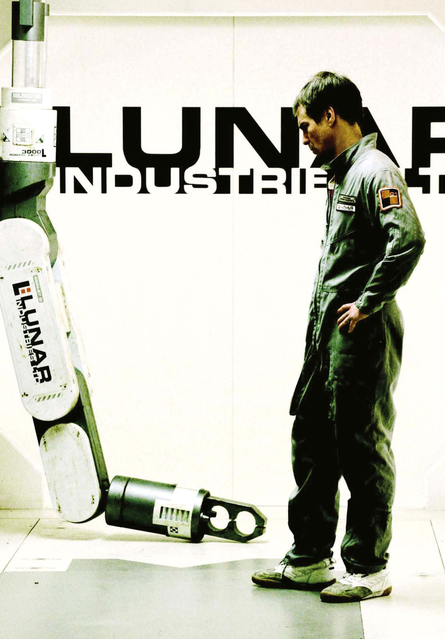 A man in a grey jumpsuit looks at a robotic arm in a white room with "LUNAR INDUSTRIES" text.