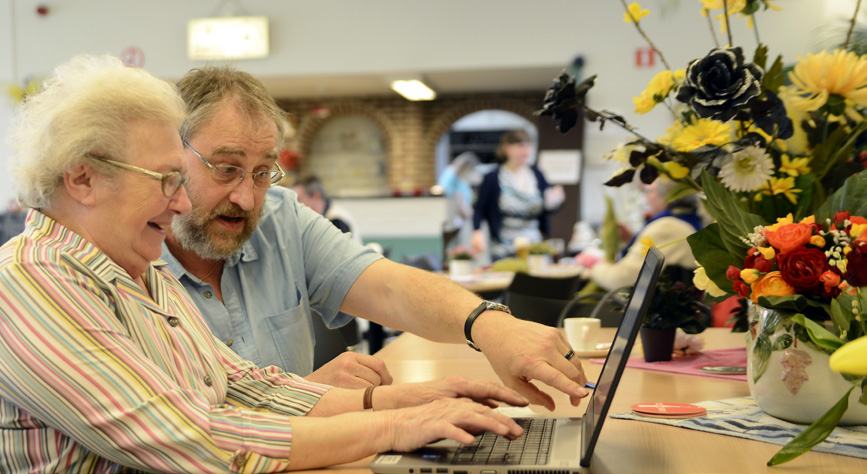 An older woman and a man looking at a laptop together, with the man pointing at the screen, in a well-lit indoor setting.