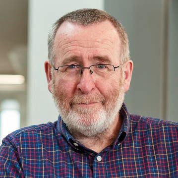 Headshot of a smiling man with a beard and glasses wearing a plaid shirt.
