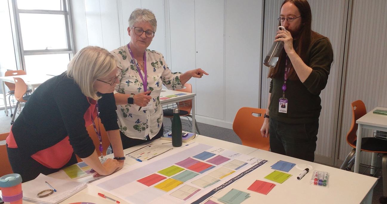 Three people collaborating around a table covered with colorful cards during a workshop or design session.